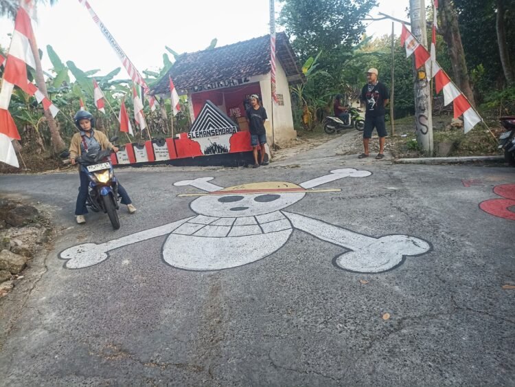 Warga melintas di samping mural bertema serial anime One Piece yang berada di Padukuhan Temuwuh Kidul, Kalurahan Balecatur, Gamping, Sleman, Rabu (6/8/2025).