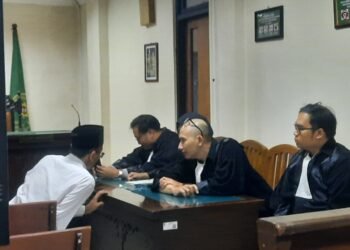 Terdakwa pembakaran tenda Polda DIY Perdana Arie Veriasa saat berbicara dengan penasehat hukumnya sebelum persidangan di Pengadilan Negeri Sleman, Senin (22/12/2025).