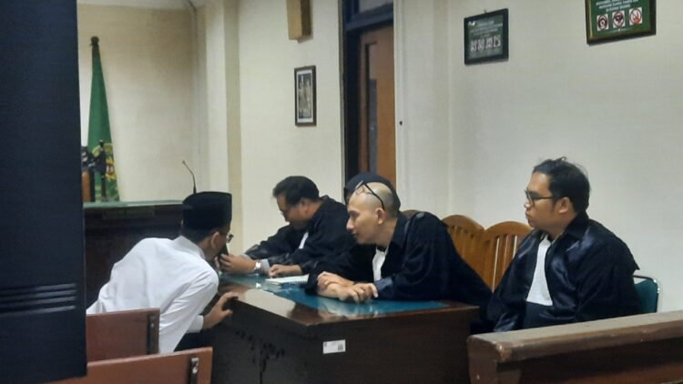 Terdakwa pembakaran tenda Polda DIY Perdana Arie Veriasa saat berbicara dengan penasehat hukumnya sebelum persidangan di Pengadilan Negeri Sleman, Senin (22/12/2025).