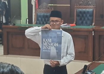 Terdakwa kasus pembakaran tenda polisi di Mapolda DIY saat mempelihatkan poster di ruang persidangan menagih janji ketua Majelis Hakim Ari Prabawa sebelum mengikuti sidang vonis, Senin (23/2/2026).
