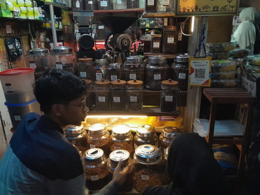 Pemilik gerai biji kopi Kios Hasanah di Pasar Beringharjo Kota Yogyakarta, Karel tengah menjelaskan perihal jenis kopi kepada pelanggan, Minggu (1/2/2026). [populi.id/Dewi Rukmini]