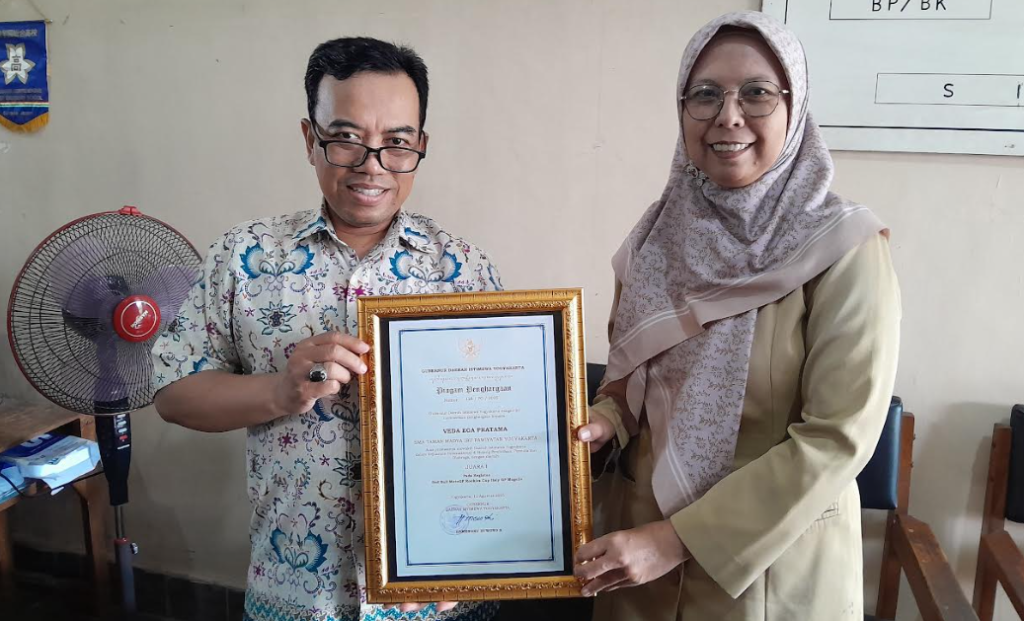 Wakil Ketua Bagian Urusan Kesiswaan SMA Taman Madya IP Yogyakarta, Ki Kadir, dan Kepala Sekolah SMA Taman Madya IP Yogyakarta, Nyi Ika Sabti Sulistyanti, menunjukkan penghargaan siswa berprestasi milik Veda Ega Pratama dari Gubernur DIY, pada Senin (2/3/2026). 