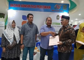Wali Kota Yogyakarta, Hasto Wardoyo (kanan), menyerahkan berkas PBG kepada warga saat kegiatan Bazar Perizinan dan Unit Reaksi Cepat Konsultasi PBG di Mall Pelayanan Publik (MPP) kompleks Balai Kota Yogyakarta, pada Selasa (2/6/2026).